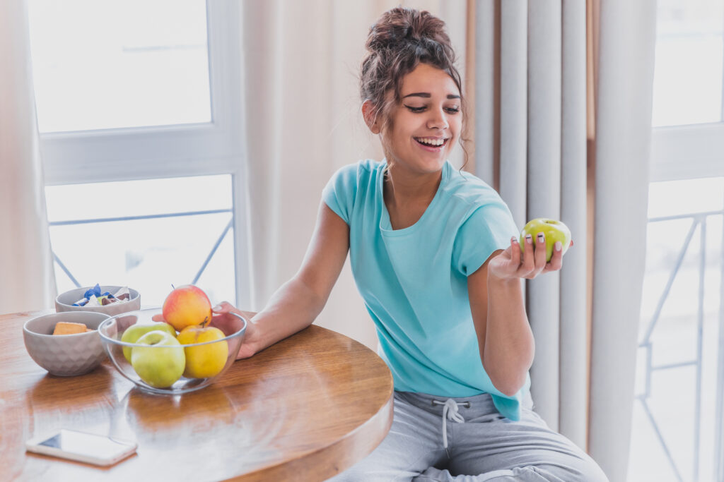 une femme regarde une pomme pour sa nutrition, qu'elle offre mybodyguard vous correspond.